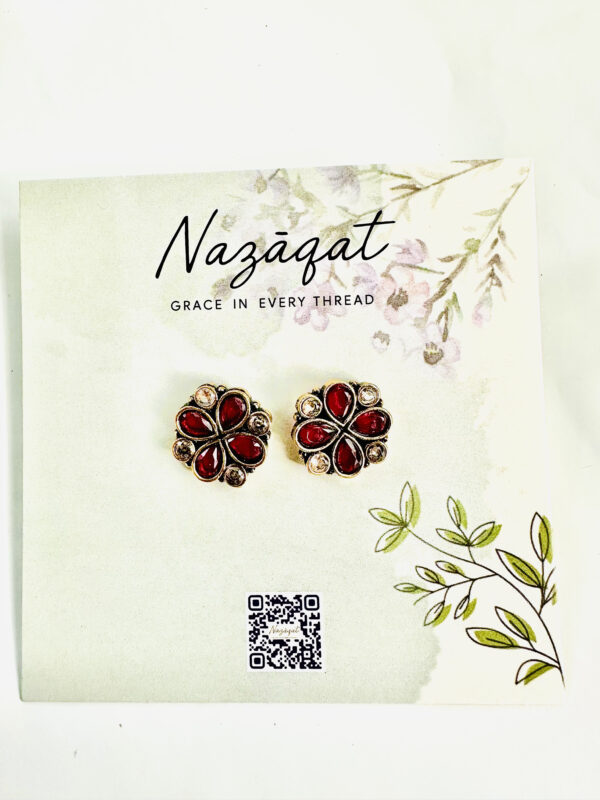 Floral oxidized silver stud earrings with red stones by Nazāqat, displayed on a soft floral backing card