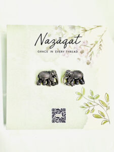 Oxidized silver elephant motif stud earrings by Nazāqat, displayed on floral backing card