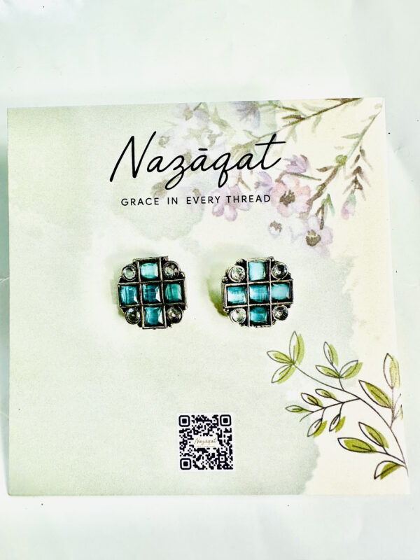 Geometric oxidized silver stud earrings with aqua blue square stones from Nazāqat, displayed on a floral card